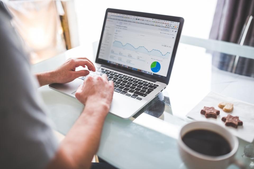 Hands typing on a laptop showing charts, next to a cup of coffee
