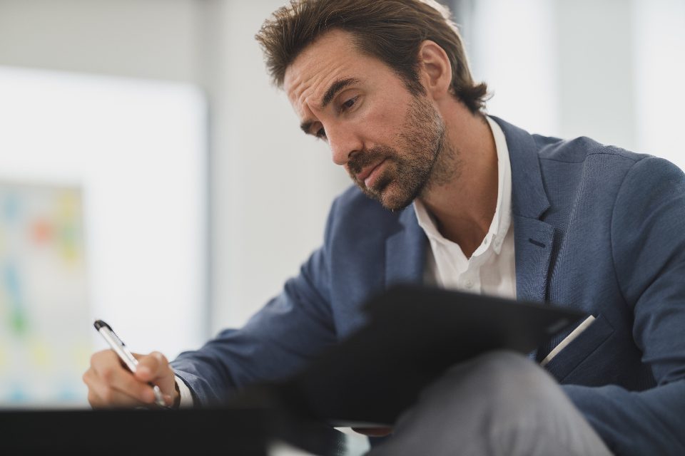 A businessman filling in a form on a clipboard at his desk